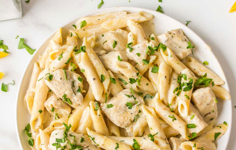 Tony’s penne pasta and chicken pieces in a creamy white sauce, garnished with fresh chopped parsley.